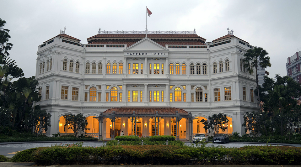As dawn breaks, the windows of Raffles Singapore glow from within, as they have done for decades.